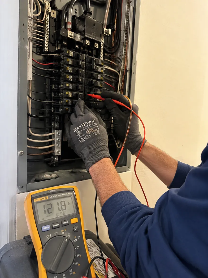 Higher Power Electric electrician testing a breaker with a Fluke multimeter reading 121.8 volts in a Denton panel