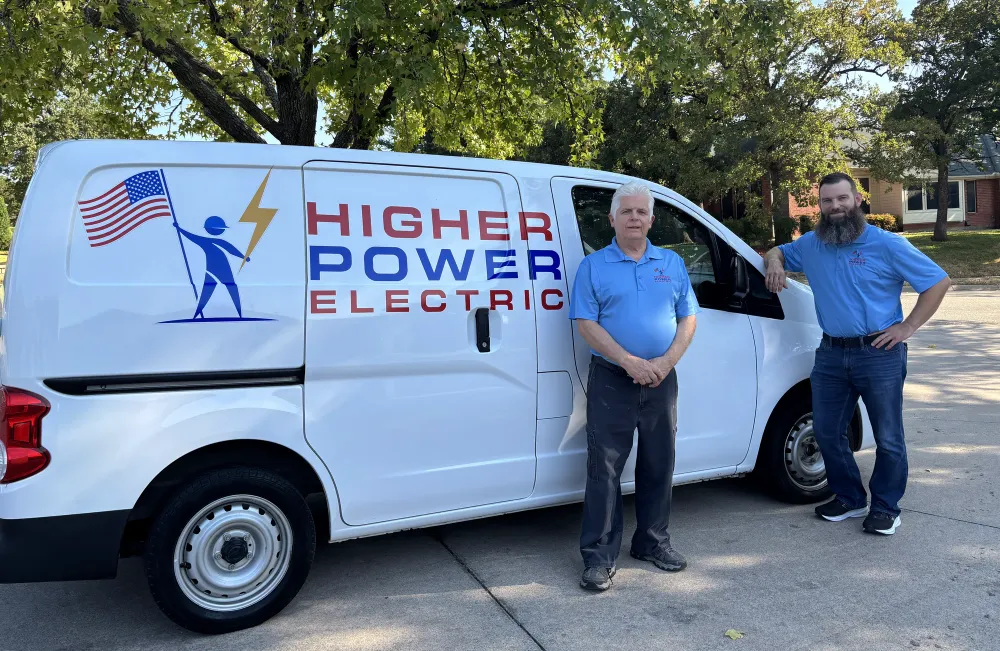 The two licensed electricians behind Higher Power Electric standing beside the company's branded service van on a residential street